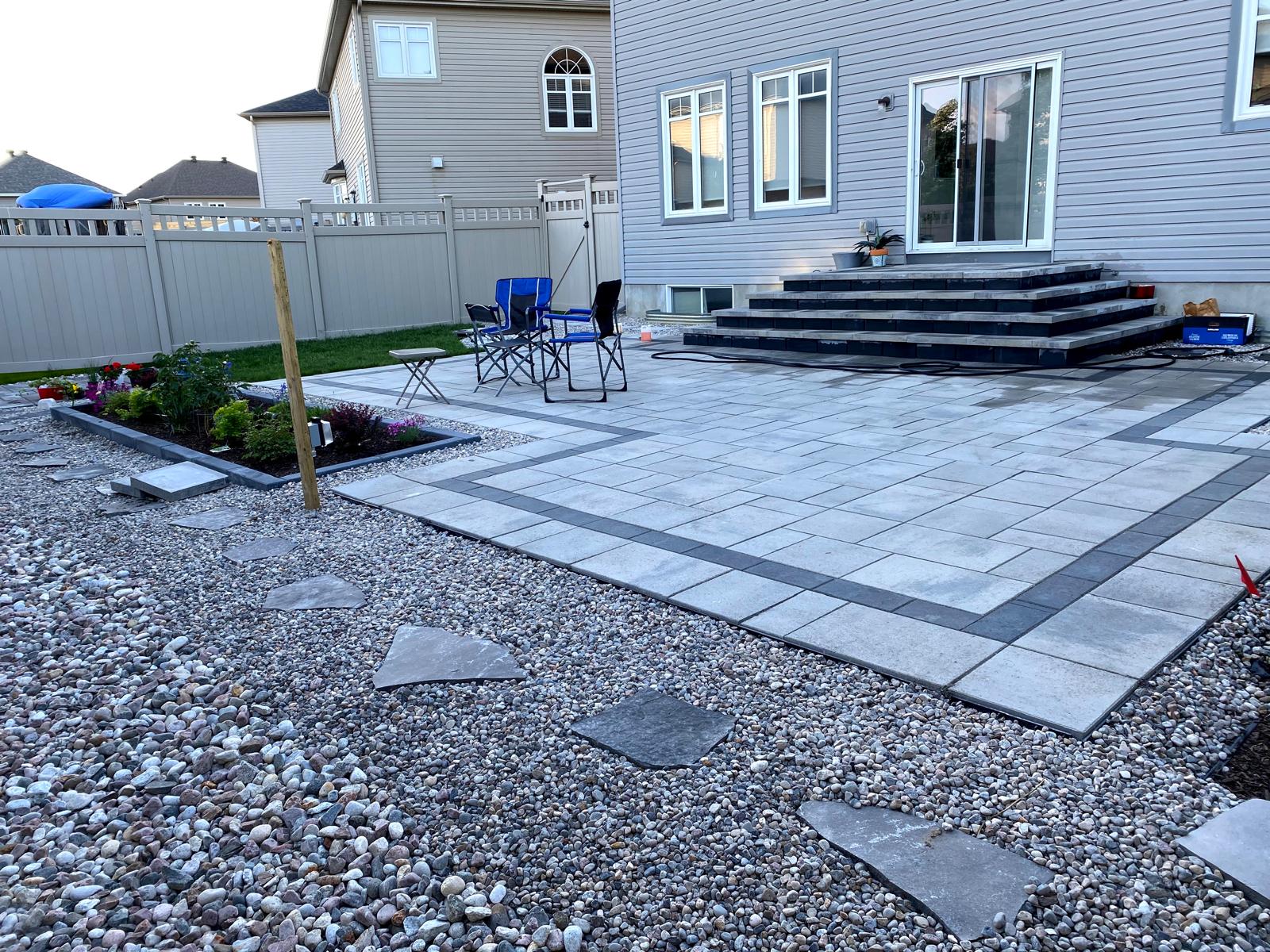 Large backyard interlocking patio with garden beds and steps